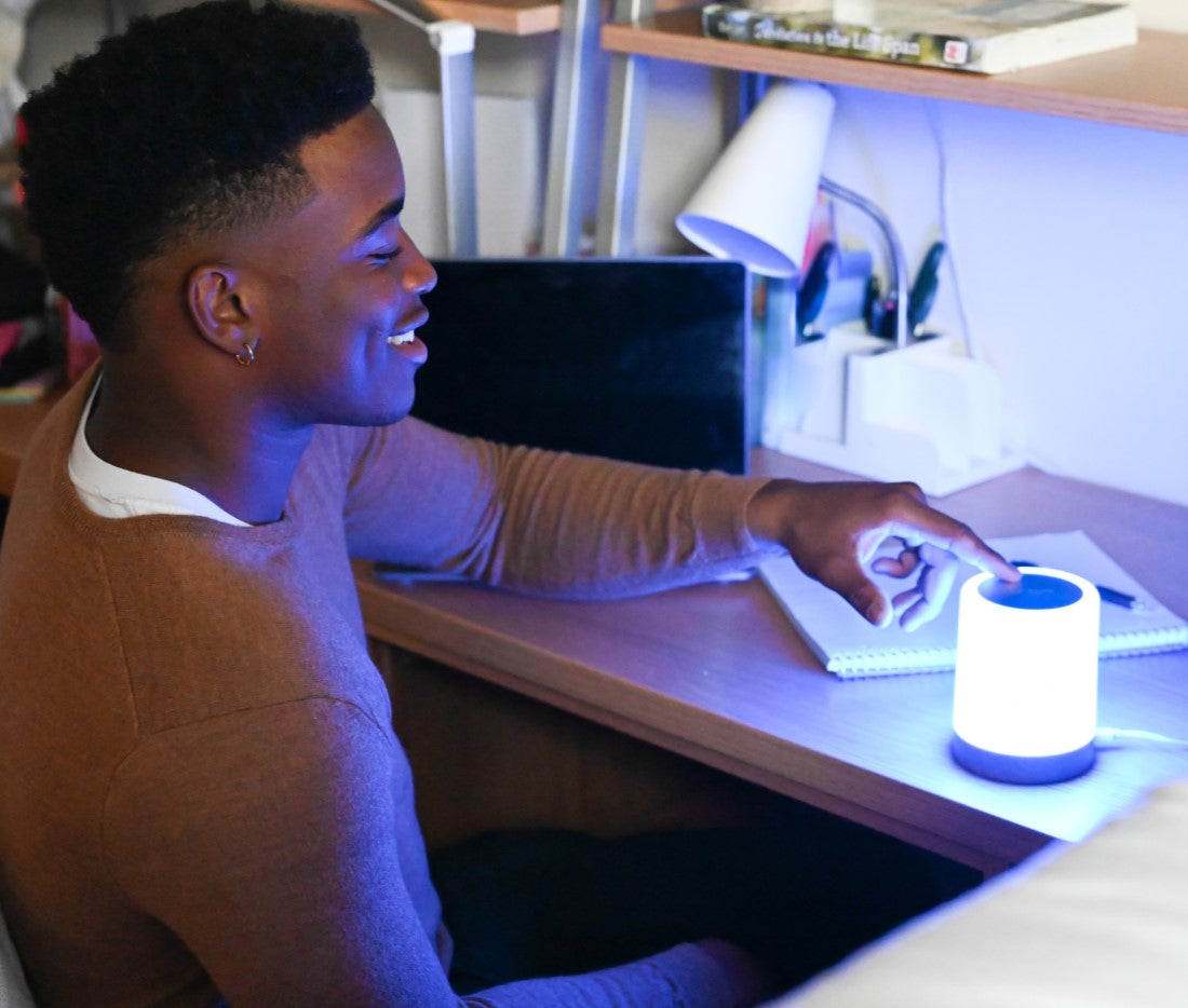 Man smiling at desk while touching a glowing LuvLink Friendship Lamp that connects him with someone remotely.