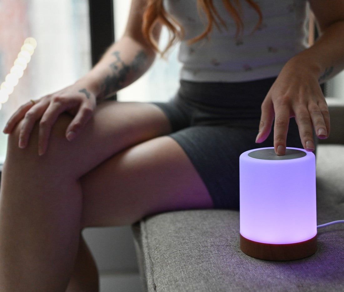 Person touching a glowing pink LuvLink Friendship Lamp while sitting, demonstrating the connected touch-activated lighting feature.